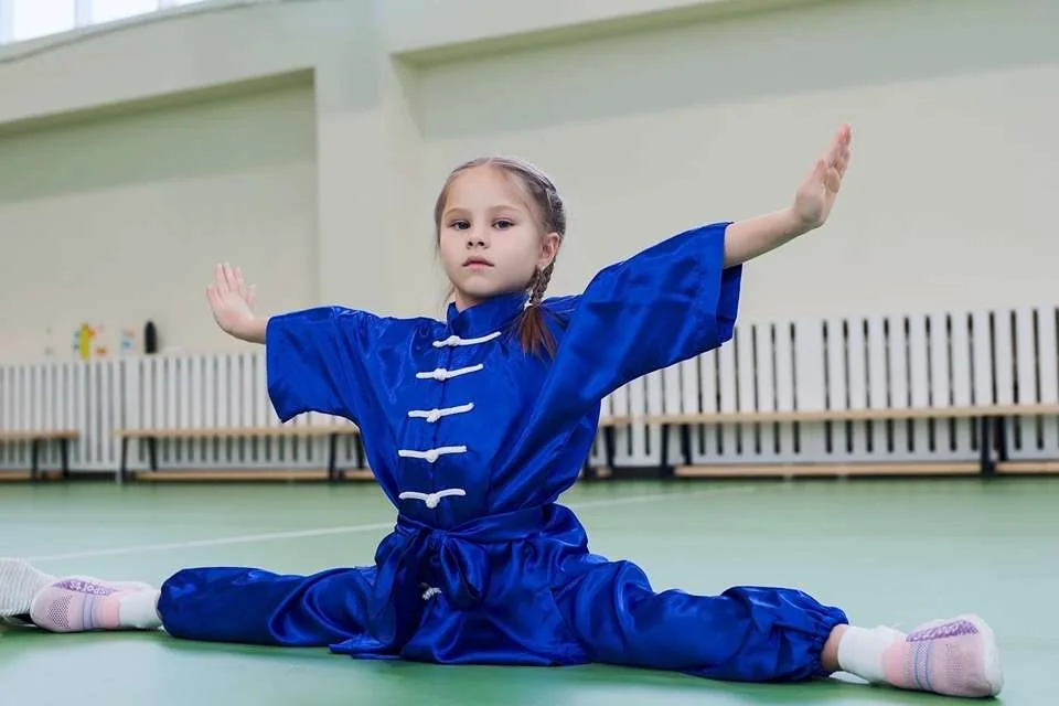 Юная спортсменка выполняет растяжку в форме ушу